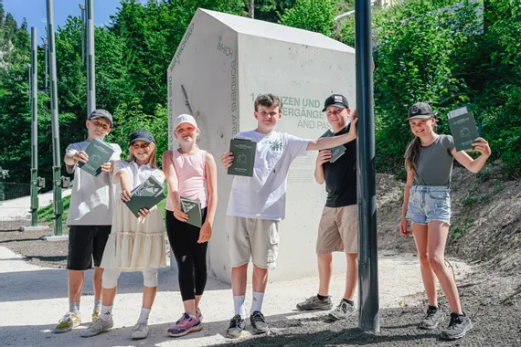 Gruppe lächelnder Kinder mit Pässen vor einer Außenausstellung zum Thema Grenzen